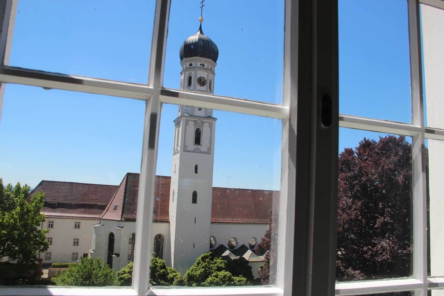 Durch ein Fenster hat man einen Blick auf das Kloster Schussenried mit seinem hohen Turm.