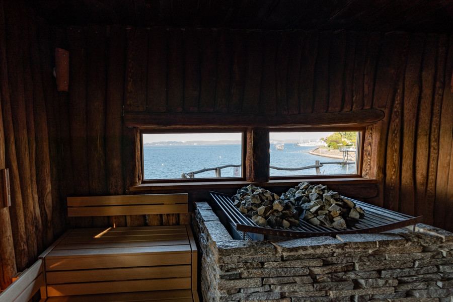 Sauna von innen in der Meersburger Therme. Neben einer Holzbank steht ein Rost auf dem heiße Steine für einen Aufguss liegen.