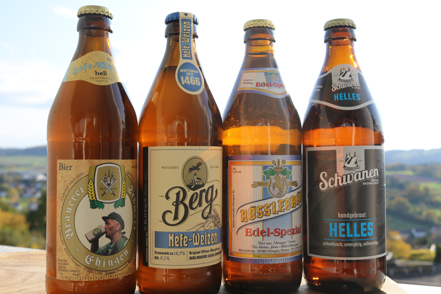 Vier verschiedene Bierflaschen stehen aufgereiht in einer Reihe.