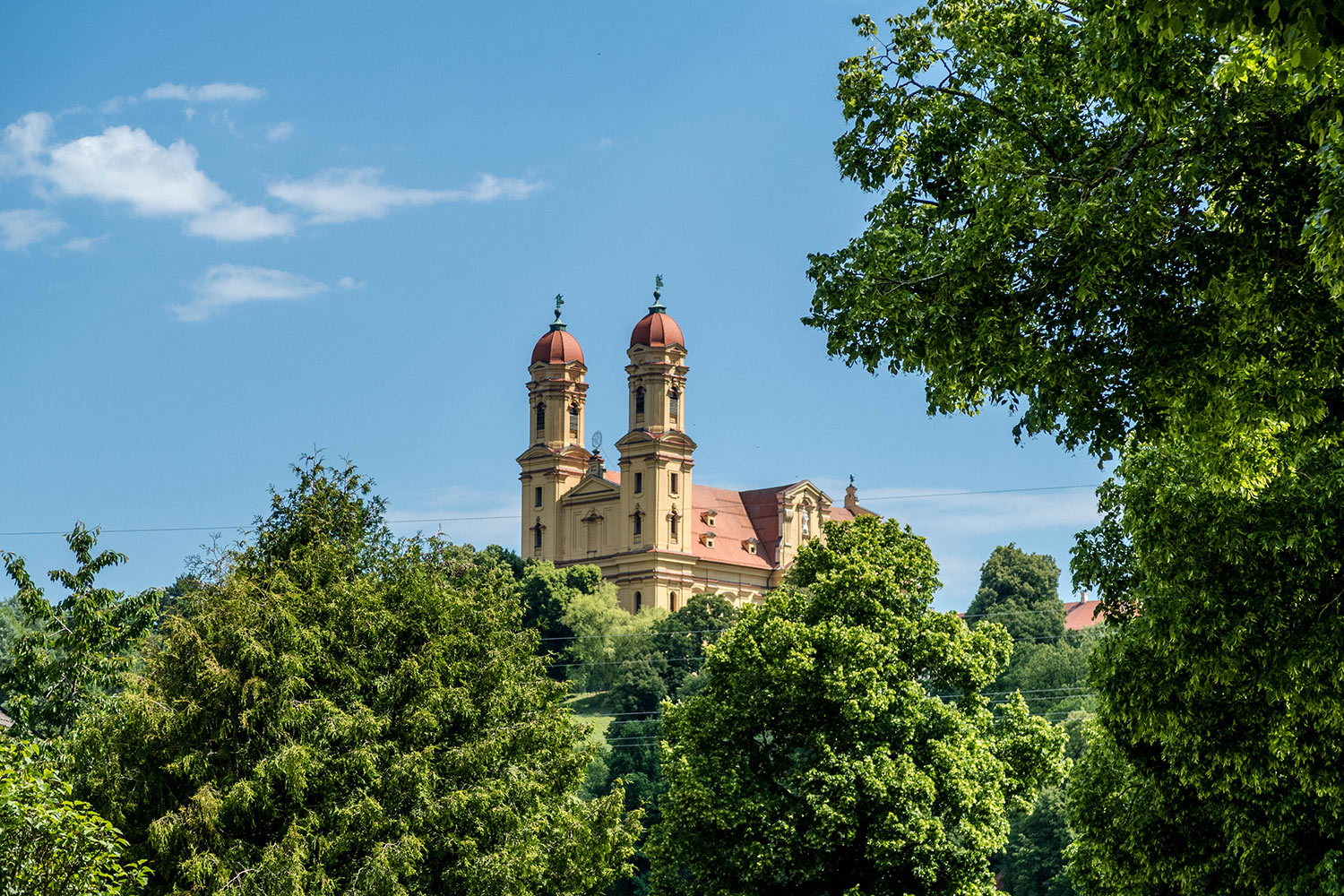 Ausblick auf die Wallfahrtskirche Schönenberg. Vor der Kirche stehen viele Bäume.