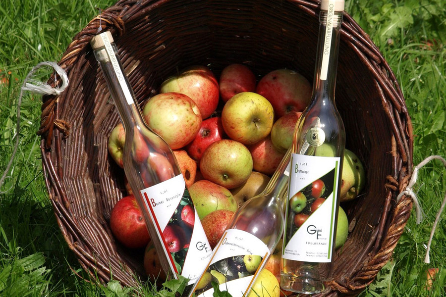 In einem großen Korb liegen viele Äpfel und drei Flaschen mit selbstgemachtem Obstbrand.