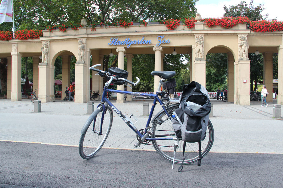 Vor dem Eingang des Stadtgarten Zoos steht ein blaues Fahrrad mit gepackten Satteltaschen.