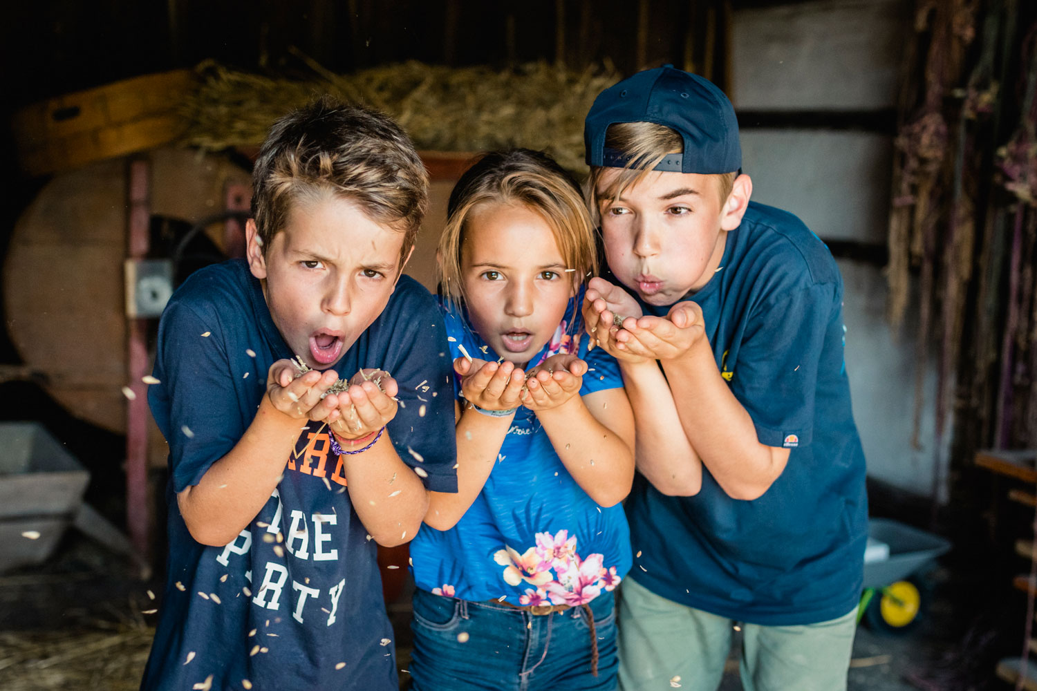 Drei Kinder stehen zusammen und pusten aus ihren Handflächen die Weizenkörner heraus.