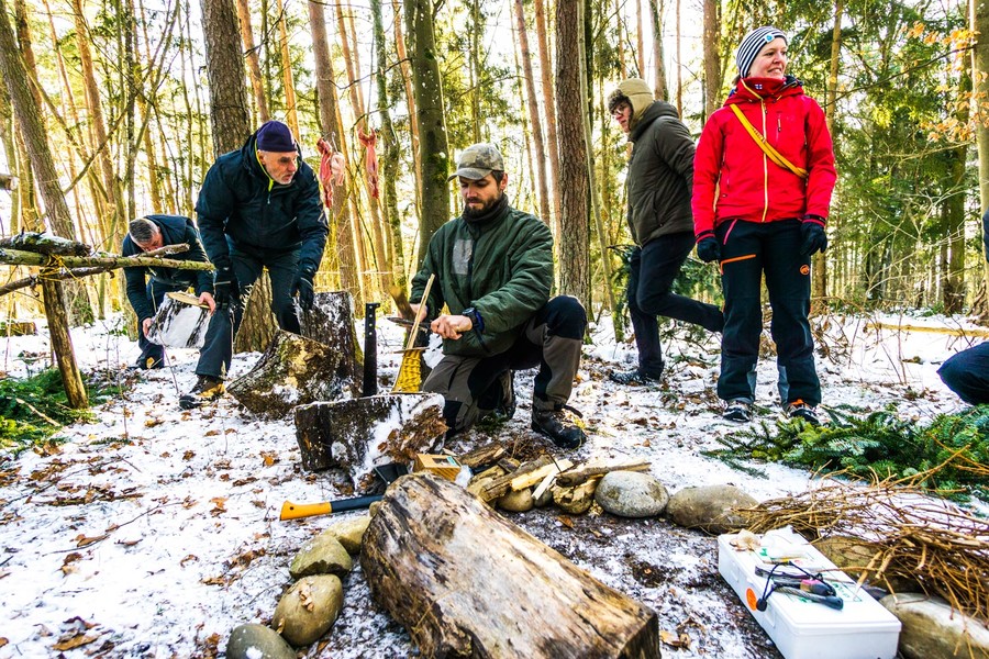 Fünf Personen sind im Winter im Schwarzwald in einem Survival-Camp. Eine Person hackt gerade Holz.
