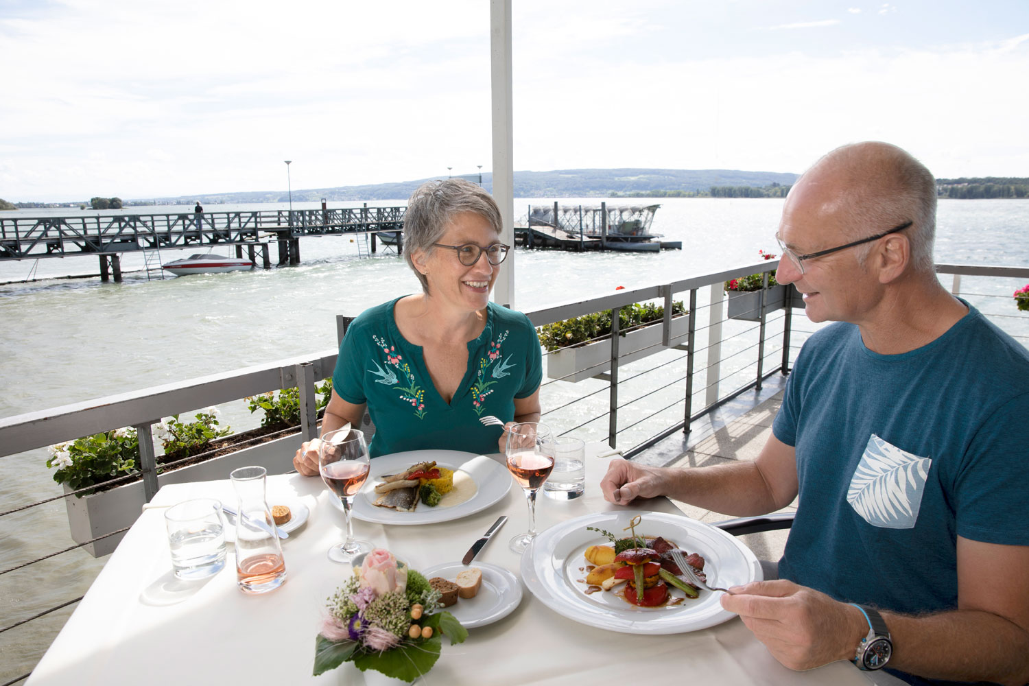 Ein etwas älteres Ehepaar genießt das Essen im Restaurant Strandcafé auf der Halbinsel Mettnau mit Blick auf den Bodensee.