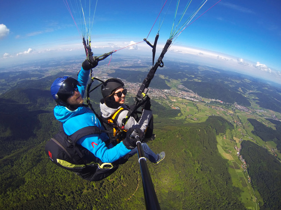 Zwei Personen fliegen zusammen mit einem Gleitschirm über den Schwarzwald.