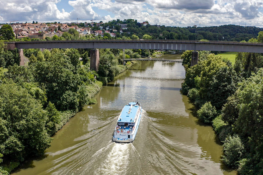 Auf dem Neckar fährt ein großes Ausflugsschiff. Eine große Brücke verläuft über dem Neckar.