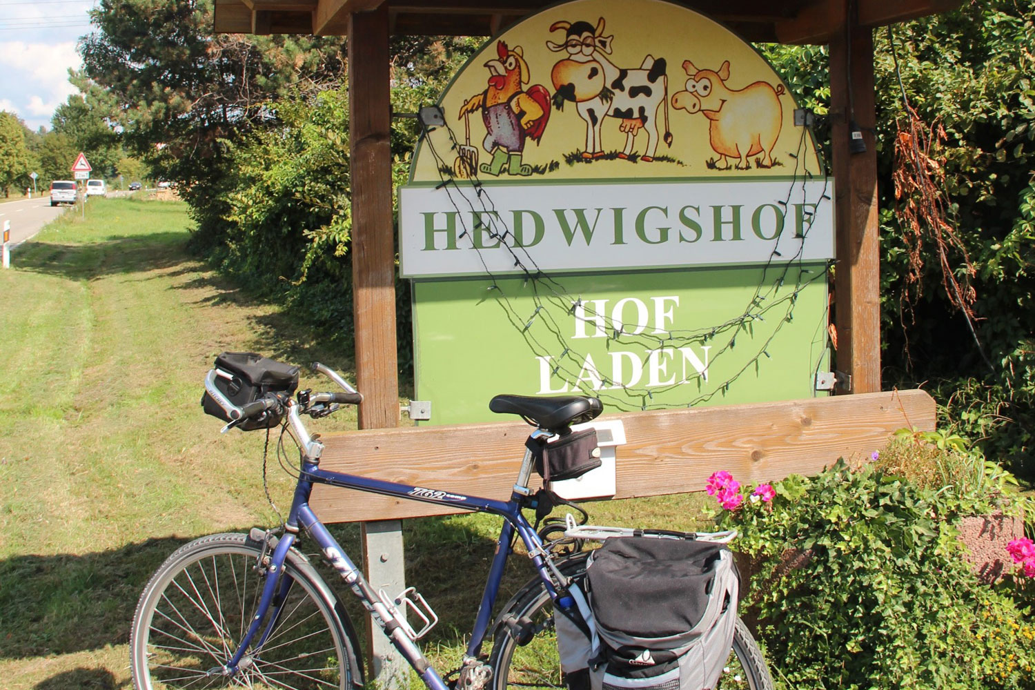Vor einem Hinweisschild mit der Aufschrift Hedwigshof Hofladen steht ein Fahrrad mit gepackten Satteltaschen.