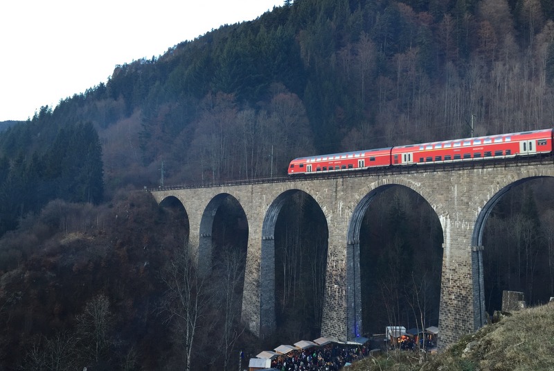 Über ein großes Viadukt fährt ein Zug, im Hintergrund sind viele Bäume.