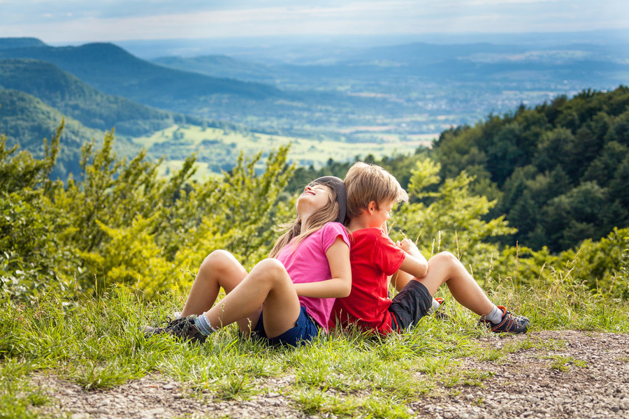 Zwei Kinder sitzen am Rande eines Wanderweges und machen eine Pause.