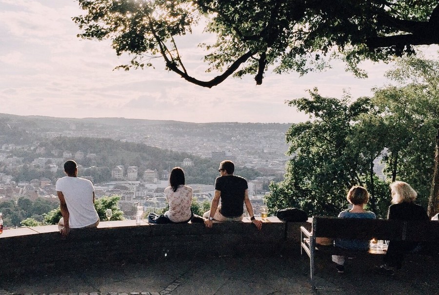 Auf einer Mauer bei einem Aussichtspunkt sitzen einige Personen und blicken hinunter auf die Stuttgarter Innenstadt.