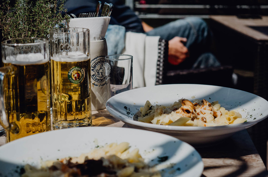 Auf einem Tisch stehen zwei Teller mit einem deftigen Gericht und zwei Gläser gefüllt mit Bier.