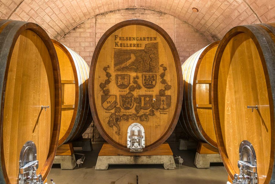 Im Keller der Weinkellerei stehen viele riesige Holzfässer die mit Wein gefüllt sind.