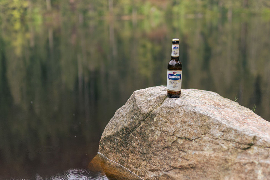 Auf einem großen Stein im Wasser steht eine Bierflasche.