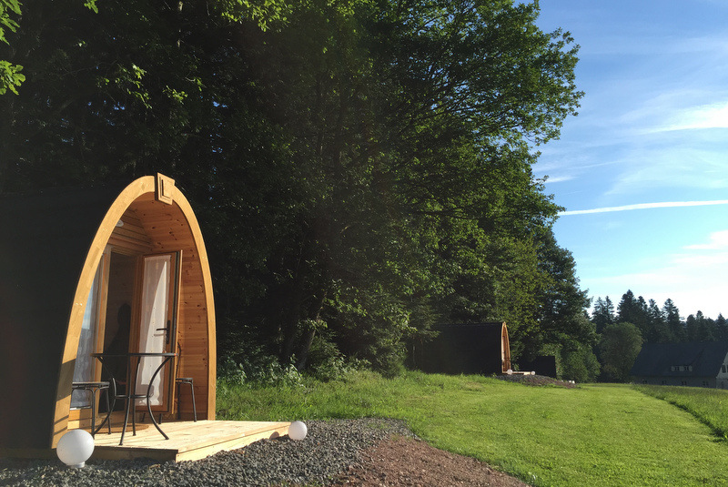 Eine ovale Campinghütte aus Holz steht auf einer Wiese.