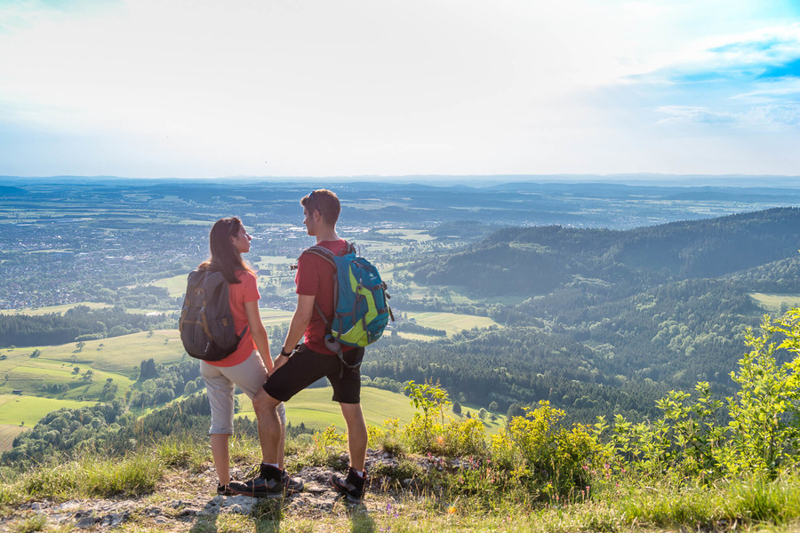 Ein Mann und eine Frau stehen in Wanderoutfits an einem Aussichtspunkt und genießen die Aussicht über die Schwäbische Alb.